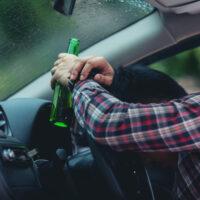 asian-man-holds-beer-bottle-while-is-driving-car